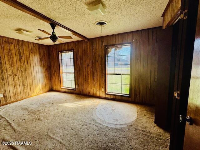 carpeted spare room with ceiling fan, a textured ceiling, visible vents, and wooden walls