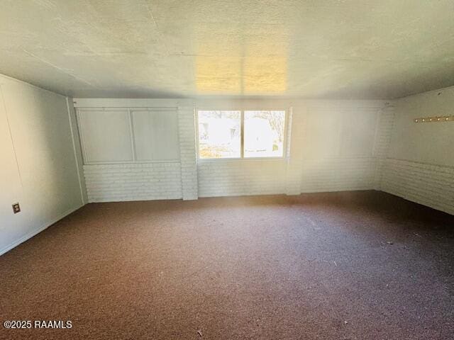 carpeted spare room featuring brick wall