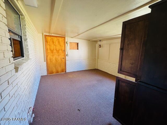 carpeted empty room featuring a large fireplace, brick wall, and beam ceiling