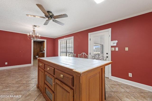 kitchen with hanging light fixtures, tile countertops, a textured ceiling, ornamental molding, and a center island