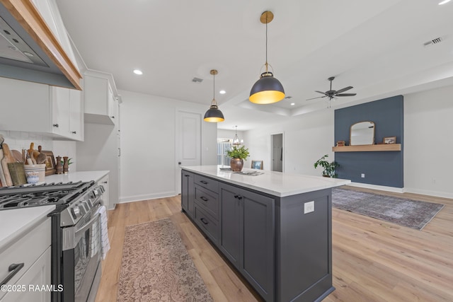 kitchen featuring custom exhaust hood, stainless steel gas stove, light wood-style flooring, white cabinetry, and visible vents