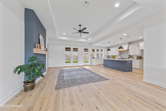 living room with a tray ceiling, light wood-type flooring, baseboards, visible vents, and recessed lighting