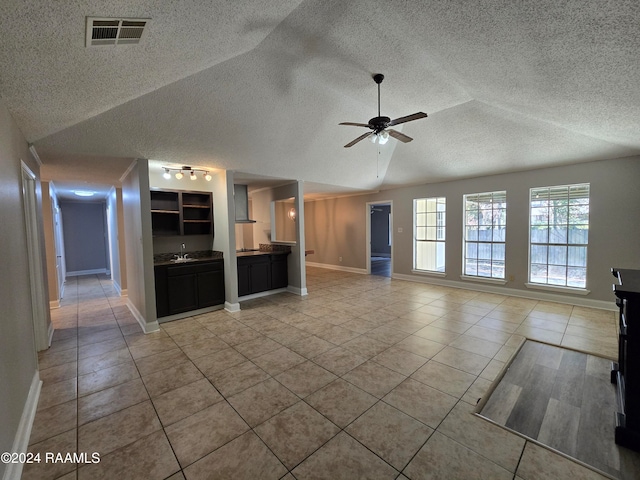 unfurnished living room with lofted ceiling, ceiling fan, a textured ceiling, sink, and tile patterned floors