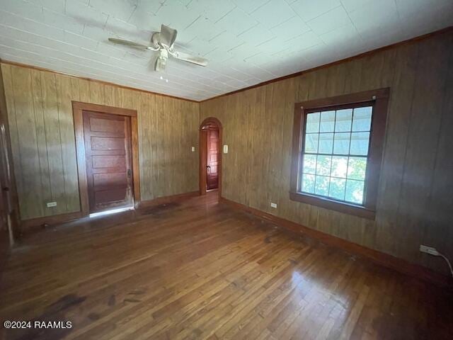 unfurnished bedroom with ceiling fan, wooden walls, and dark hardwood / wood-style flooring