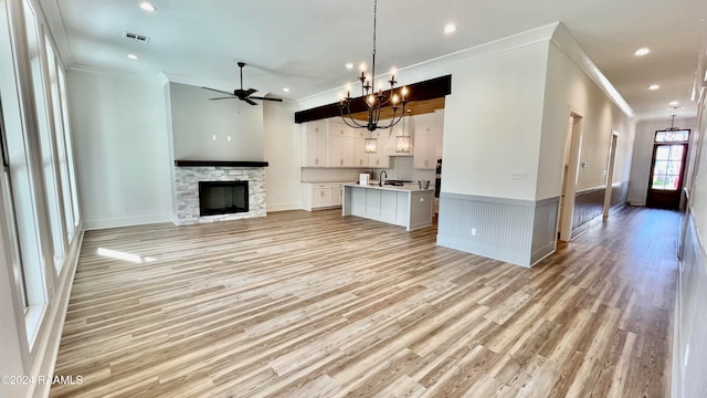 unfurnished living room featuring ceiling fan with notable chandelier, light wood-type flooring, and ornamental molding