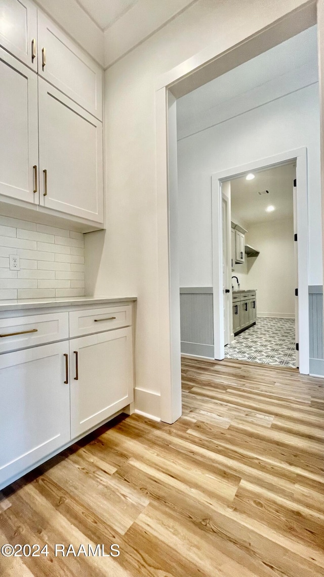 bar featuring decorative backsplash, light hardwood / wood-style floors, and white cabinetry