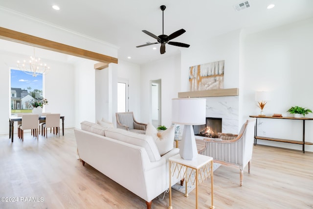 living room featuring ceiling fan with notable chandelier, a fireplace, and light hardwood / wood-style flooring