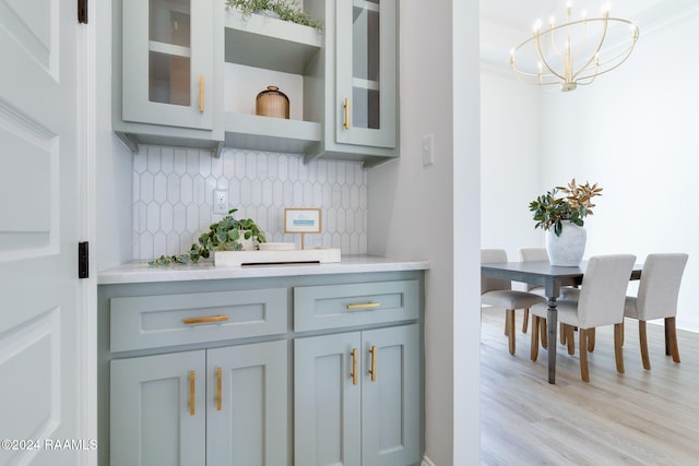 bar featuring pendant lighting, backsplash, crown molding, a notable chandelier, and light hardwood / wood-style floors