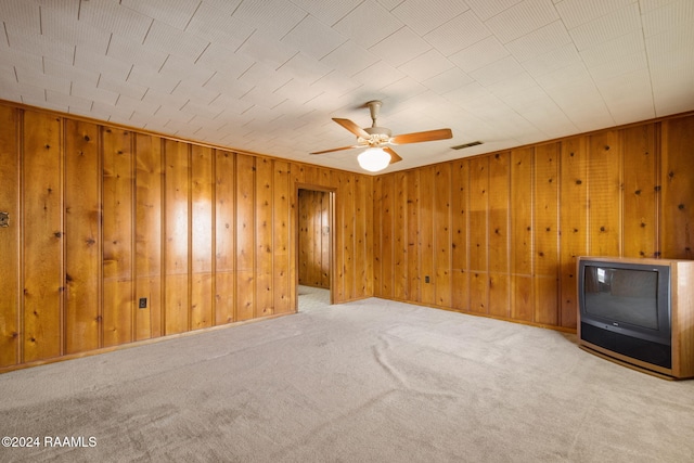 spare room with ceiling fan, wood walls, and carpet flooring