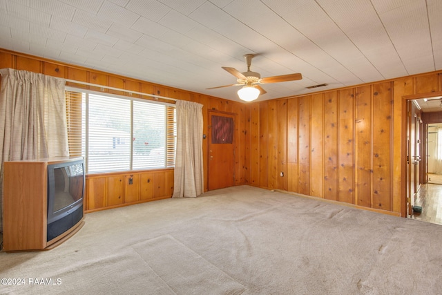 carpeted empty room with ceiling fan and wooden walls