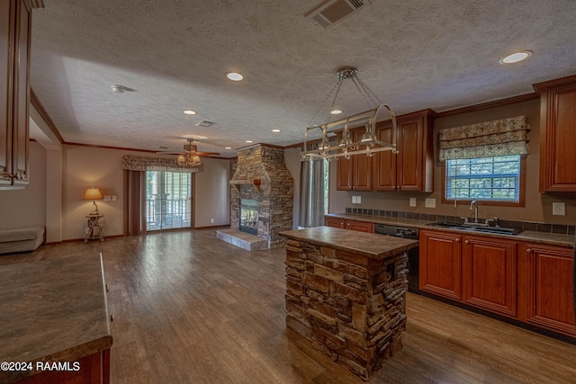 kitchen featuring sink, a stone fireplace, a textured ceiling, a center island, and hardwood / wood-style flooring