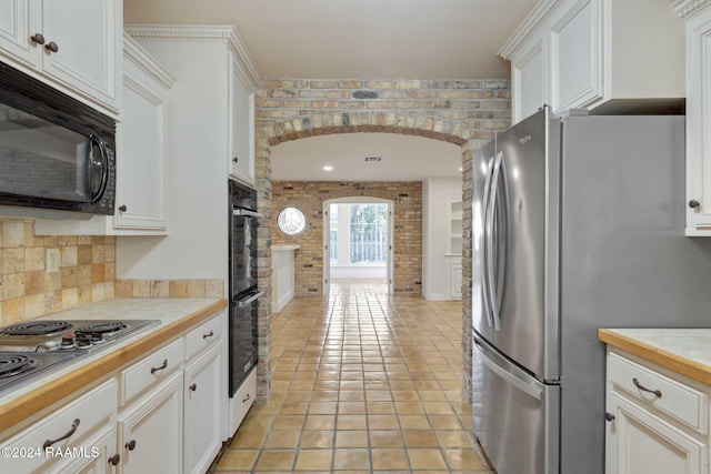 kitchen with brick wall, white cabinetry, stainless steel appliances, and light tile patterned floors