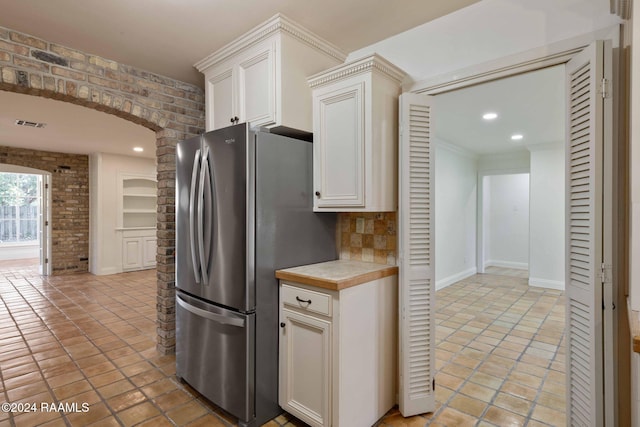 kitchen featuring brick wall, stainless steel fridge, white cabinetry, and light tile patterned floors