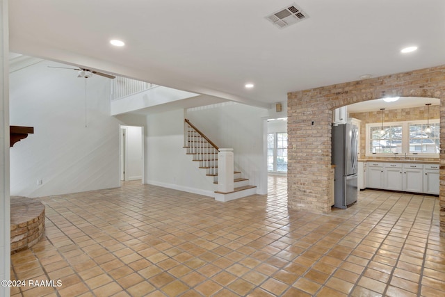 unfurnished living room featuring brick wall, light tile patterned flooring, and ceiling fan