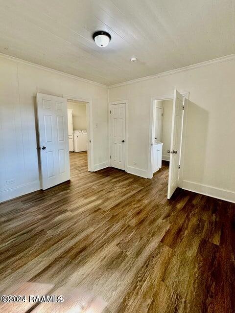 unfurnished bedroom featuring dark wood-type flooring, ornamental molding, and separate washer and dryer