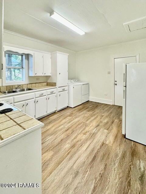 kitchen featuring sink, light wood-type flooring, white cabinetry, washer and dryer, and white appliances