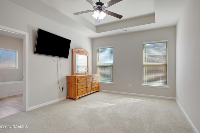 unfurnished bedroom featuring light carpet, multiple windows, a raised ceiling, and ceiling fan