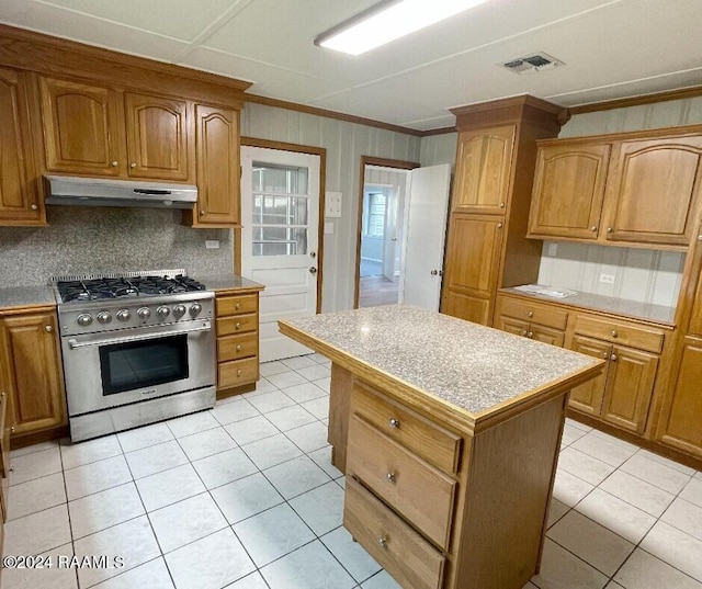 kitchen featuring backsplash, ornamental molding, a center island, stainless steel stove, and light tile patterned flooring