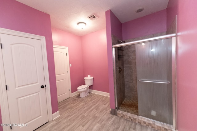 bathroom featuring toilet, a textured ceiling, hardwood / wood-style flooring, and a shower with shower door