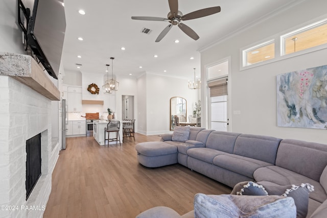 living room featuring a stone fireplace, ornamental molding, light wood-type flooring, and ceiling fan with notable chandelier