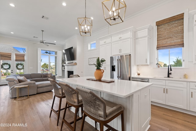 kitchen with a kitchen island, hanging light fixtures, white cabinets, a kitchen bar, and appliances with stainless steel finishes