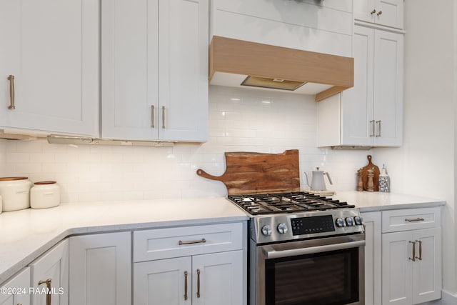 kitchen with custom range hood, backsplash, light stone countertops, white cabinets, and gas stove