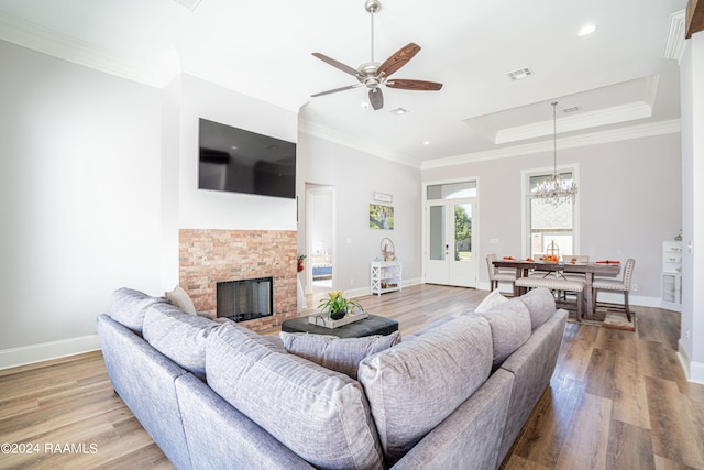 living room with french doors, wood-type flooring, crown molding, a fireplace, and ceiling fan with notable chandelier