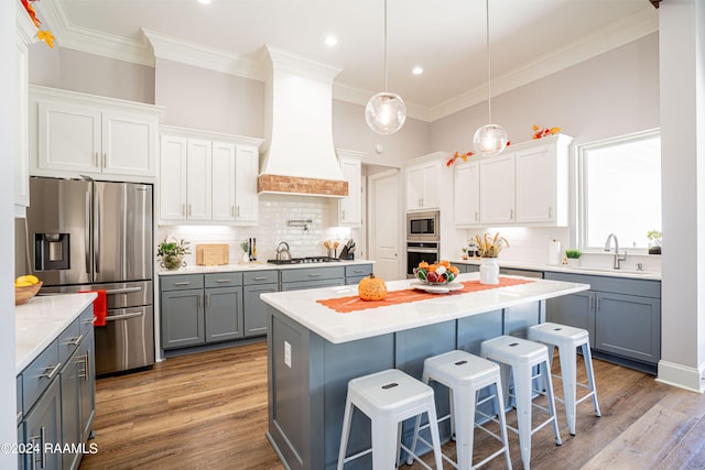 kitchen featuring appliances with stainless steel finishes, a center island, light hardwood / wood-style floors, white cabinets, and custom range hood