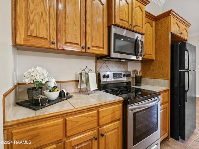 kitchen featuring tile countertops, stainless steel appliances, crown molding, light tile patterned floors, and tasteful backsplash