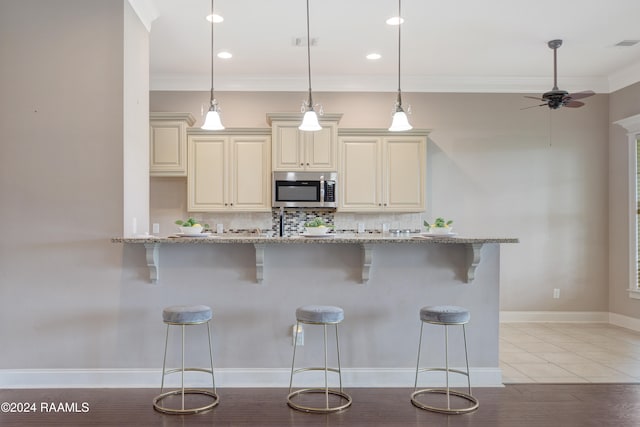 kitchen featuring light hardwood / wood-style floors, cream cabinets, light stone counters, a kitchen bar, and decorative light fixtures