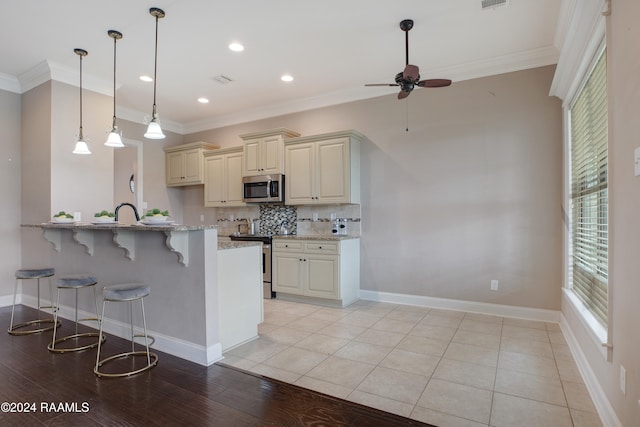 kitchen featuring stainless steel appliances, light hardwood / wood-style floors, cream cabinets, ornamental molding, and light stone countertops