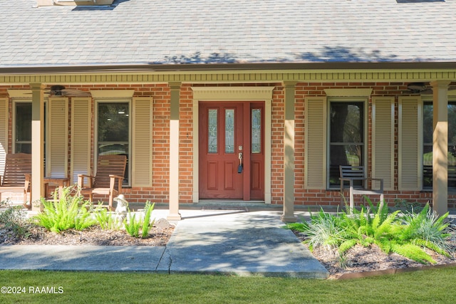 view of exterior entry with a porch, brick siding, and roof with shingles