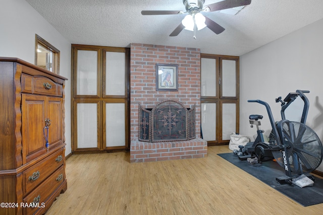 exercise area with a fireplace, a textured ceiling, ceiling fan, and light wood-style floors