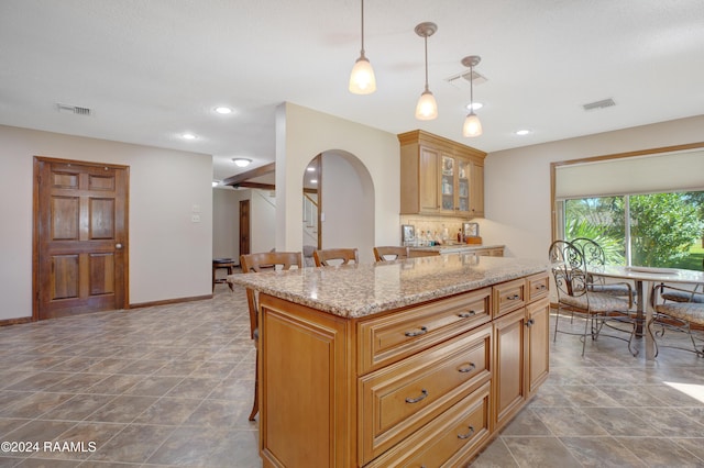 kitchen with visible vents, a kitchen bar, light stone counters, arched walkways, and hanging light fixtures