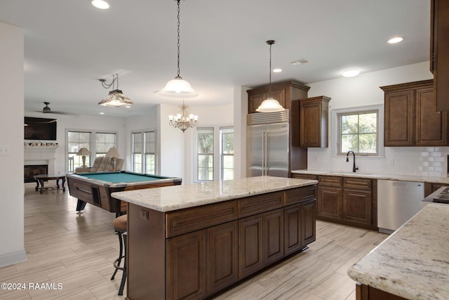 kitchen featuring sink, a kitchen island, stainless steel appliances, decorative light fixtures, and billiards