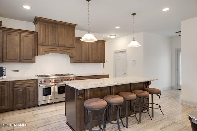 kitchen with decorative backsplash, light stone counters, a center island, range with two ovens, and decorative light fixtures