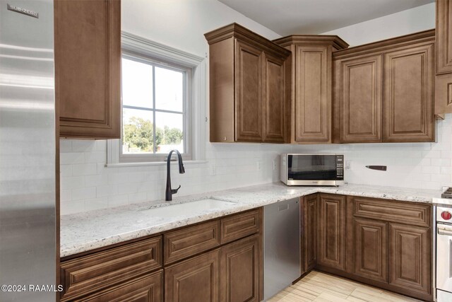 kitchen with light stone counters, stainless steel appliances, sink, and backsplash