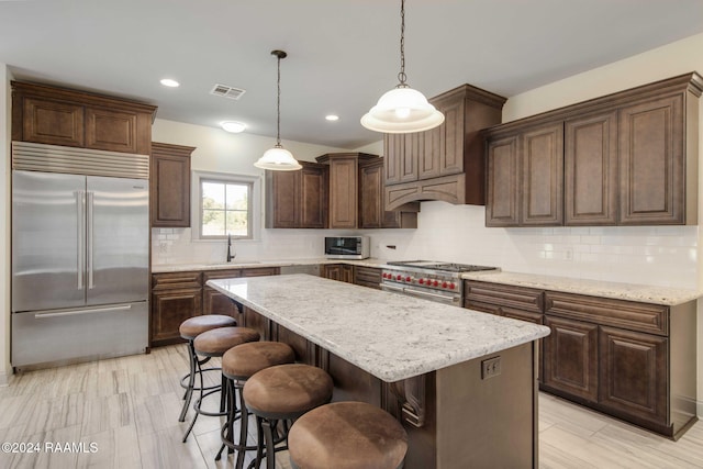 kitchen featuring premium appliances, light stone countertops, sink, a kitchen island, and hanging light fixtures