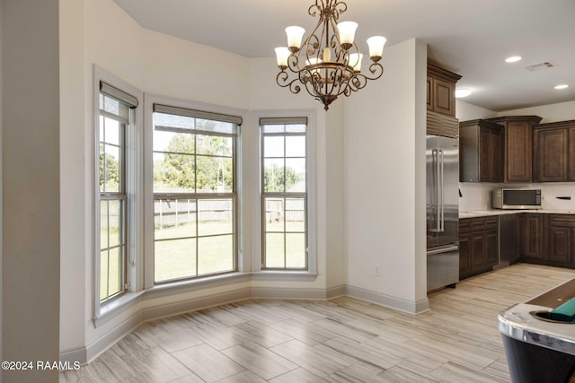 kitchen featuring dark brown cabinetry, appliances with stainless steel finishes, decorative light fixtures, and an inviting chandelier