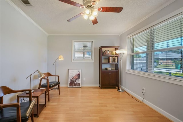 sitting room with light wood finished floors, crown molding, visible vents, and a textured ceiling