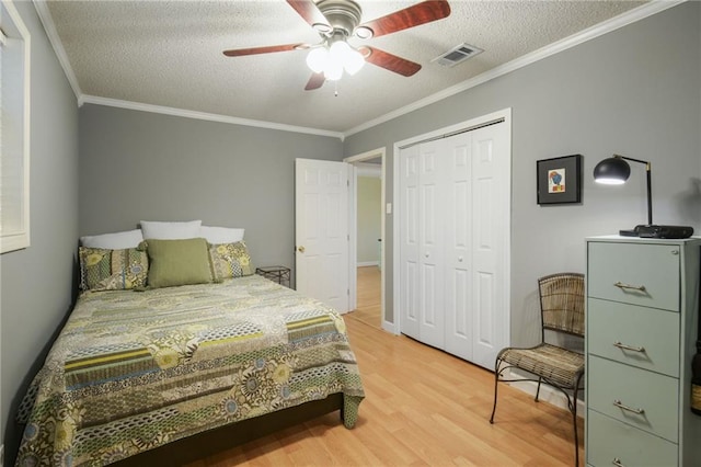 bedroom with light wood finished floors, visible vents, ornamental molding, a textured ceiling, and a closet