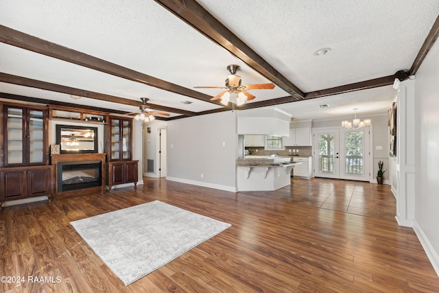 unfurnished living room with french doors, beam ceiling, a textured ceiling, ceiling fan with notable chandelier, and dark hardwood / wood-style flooring