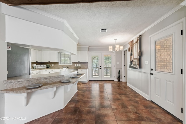 kitchen featuring kitchen peninsula, hanging light fixtures, a kitchen breakfast bar, white cabinetry, and crown molding