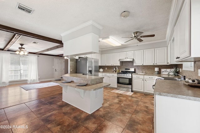 kitchen with appliances with stainless steel finishes, a kitchen bar, a textured ceiling, white cabinetry, and beam ceiling