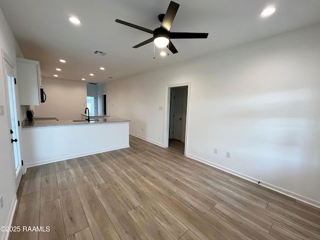 unfurnished living room with ceiling fan, sink, and light wood-type flooring