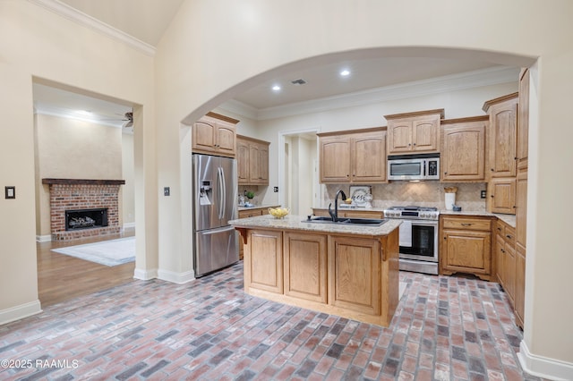 kitchen featuring appliances with stainless steel finishes, an island with sink, sink, backsplash, and ornamental molding