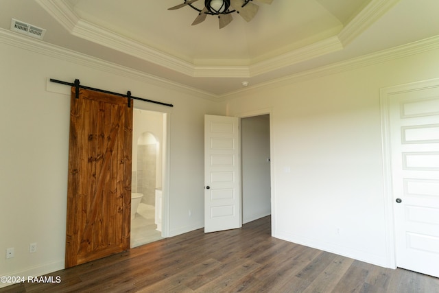 unfurnished bedroom with ensuite bath, ornamental molding, a tray ceiling, dark wood-type flooring, and a barn door