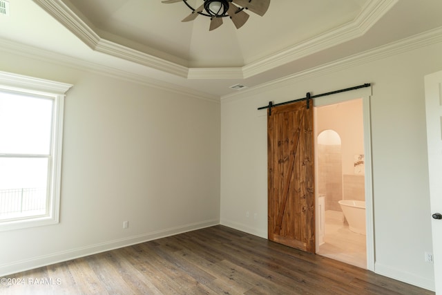 empty room featuring ceiling fan, a barn door, ornamental molding, a tray ceiling, and dark hardwood / wood-style flooring