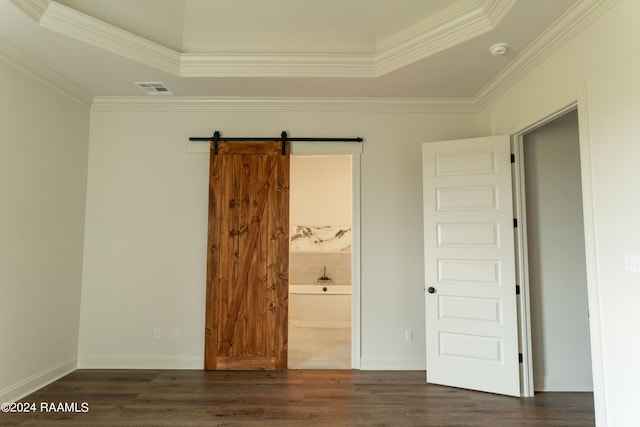 unfurnished bedroom with ensuite bathroom, ornamental molding, a raised ceiling, dark wood-type flooring, and a barn door