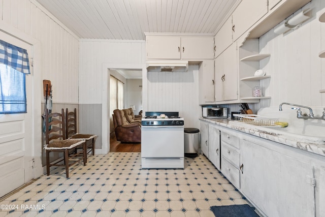 kitchen featuring white gas range, white cabinetry, sink, crown molding, and wood walls